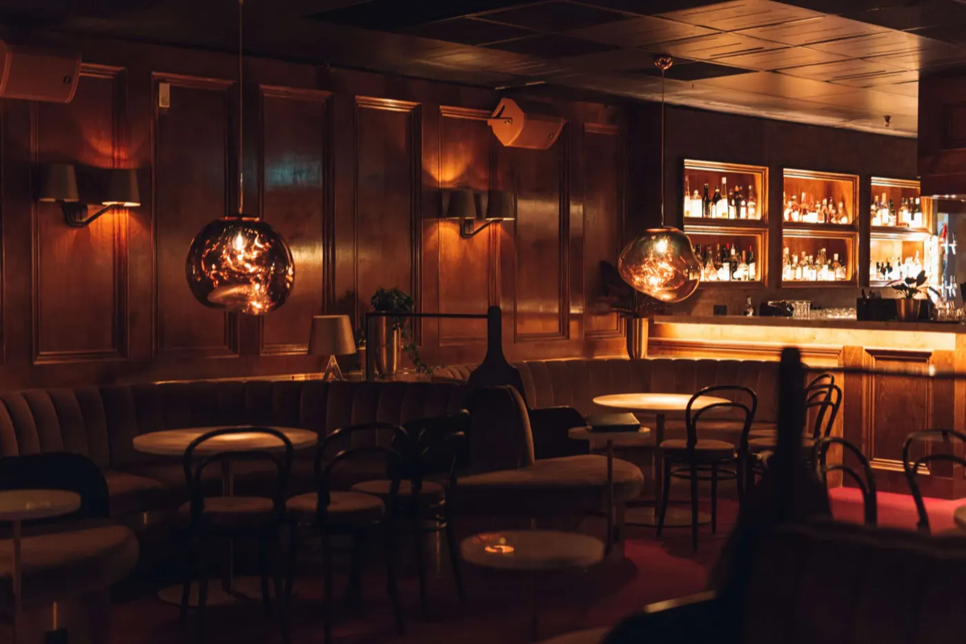 Lounge med mörk träpanel, rund soffbänk, klotformade lampor och bardisk i fonden