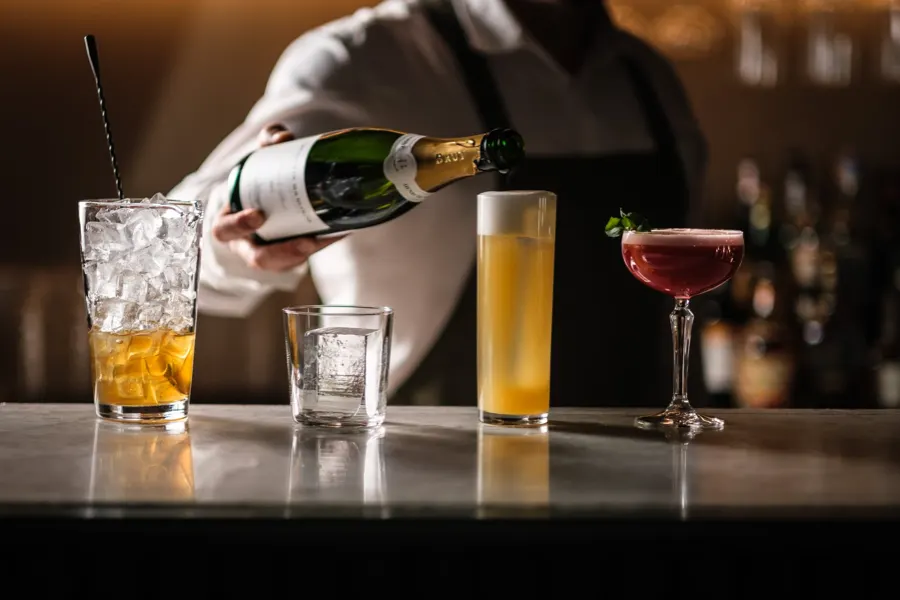 Bartender som häller mousserande vin bredvid uppradade drinkar på en bardisk