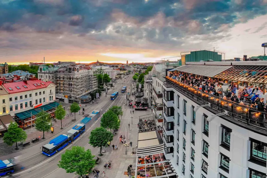 Vy uppifrån över en bred aveny i skymning, med den fullsatta takterrassen till höger
