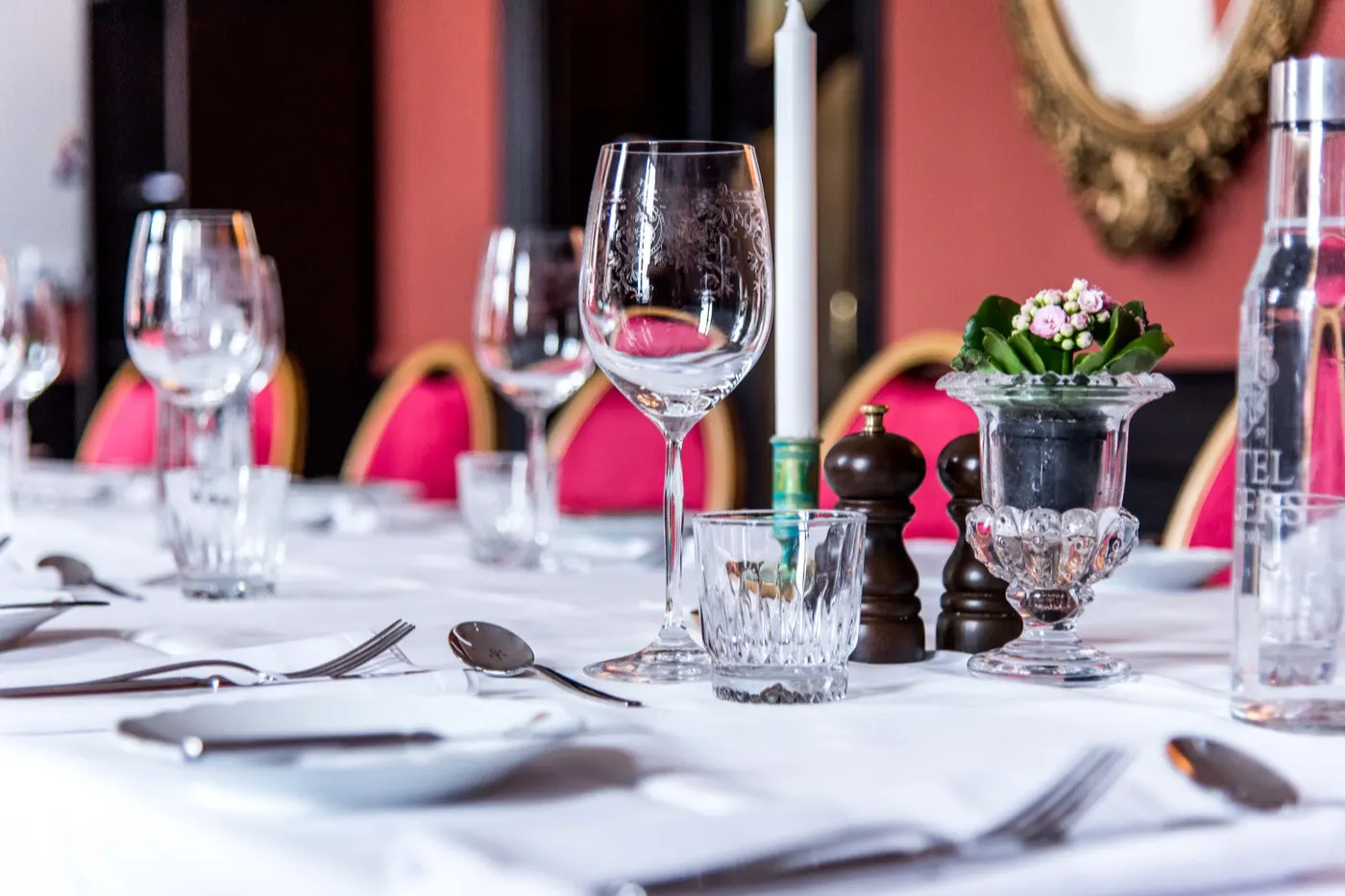 Dukat bord med vitt linne, tända ljus och rosa stolar framför en förgylld spegel