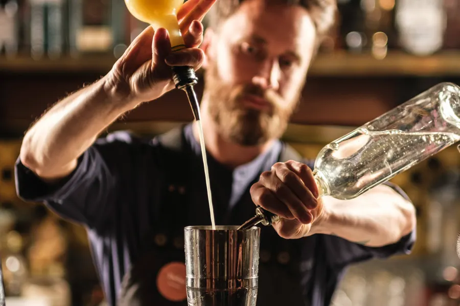Bartender som häller upp en drink bakom en bardisk med flaskhyllor