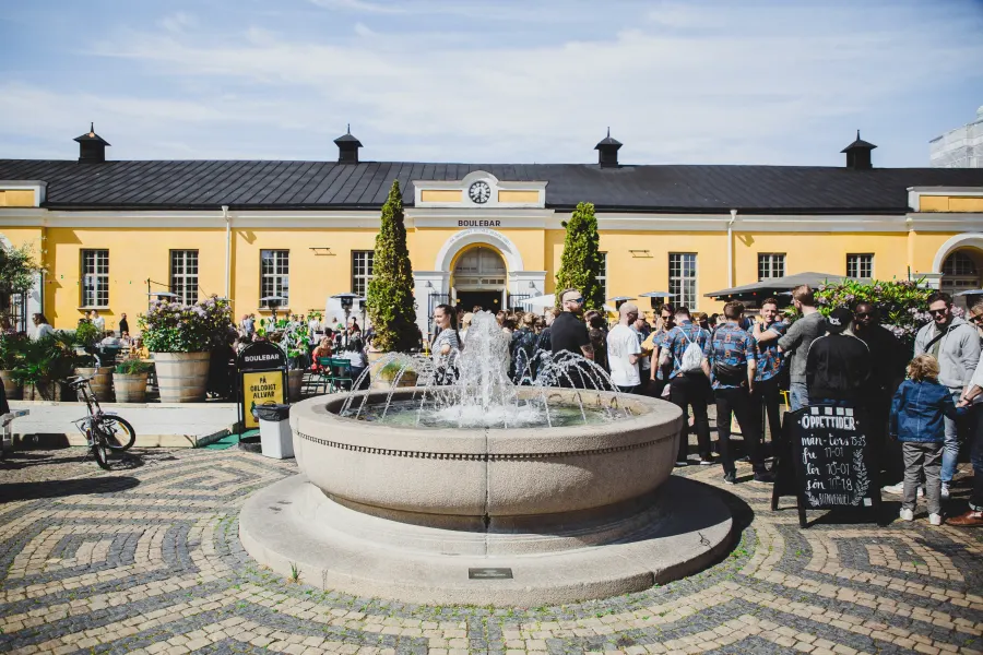 Fontän på en kullerstensgård framför den gula byggnaden med gäster utanför