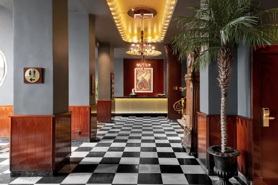 Hotellobby med svartvitt marmorgolv, mahognypaneler, ljuskrona och palm i kruka