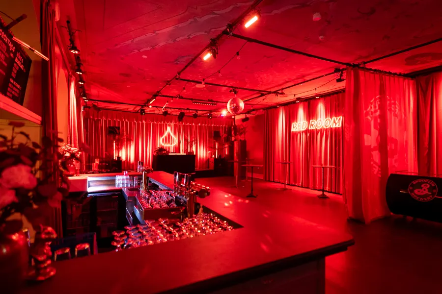 Bar i rött ljus med draperier, discokula och en neonskylt på väggen