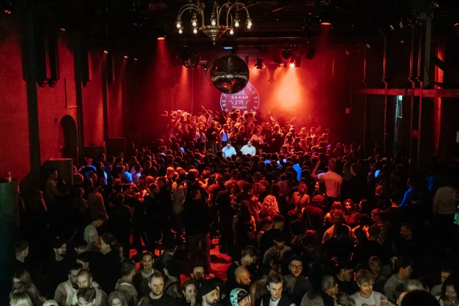 Fullsatt salong sedd uppifrån med publik framför en scen under en discokula