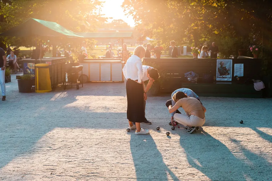 Sällskap som spelar boule på grus i motljus en sommarkväll