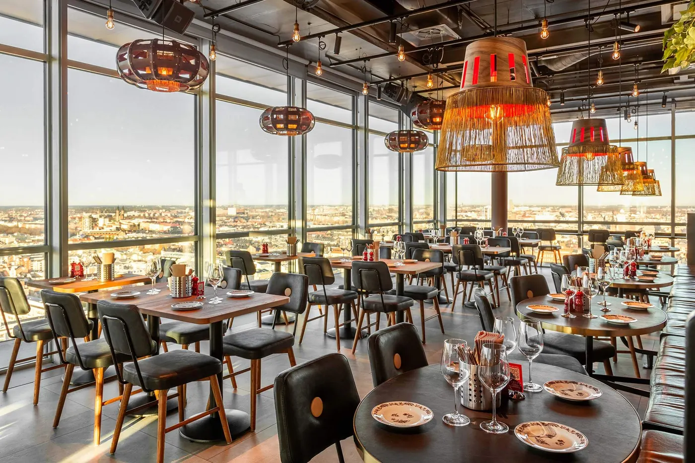 Matsal med panoramafönster och lampor i tak högt över staden